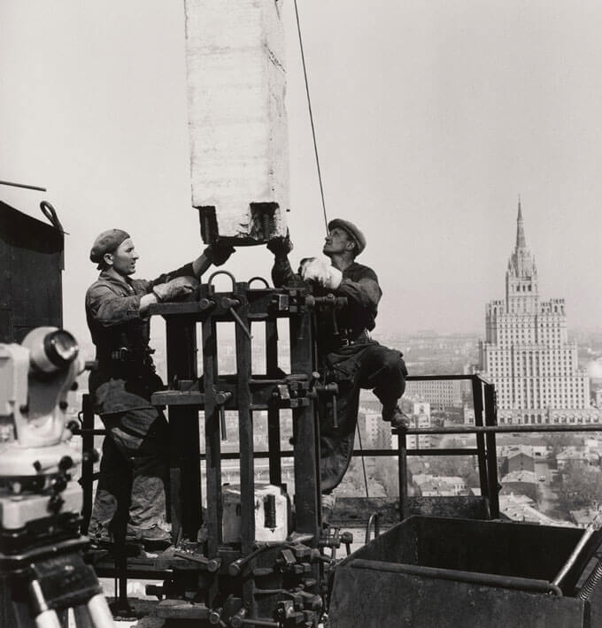 A photo of two construction workers building a skyskraper.
