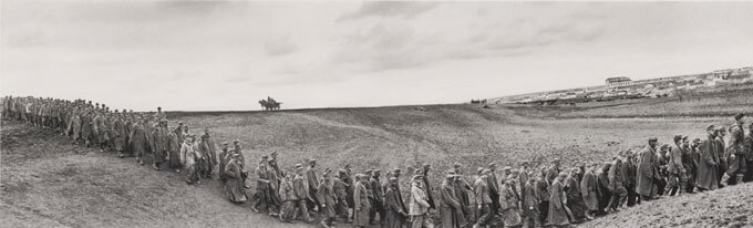 Black and white photo of POWs marching in a long line across a rural setting.