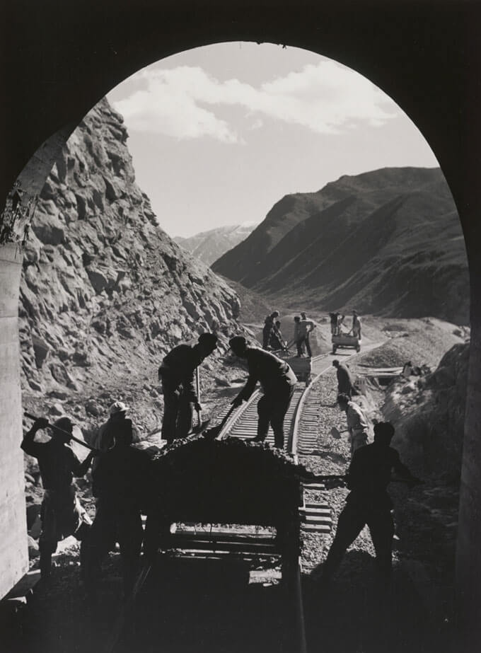 A black and white photo of workers building a railroad, framed by a tunnel.