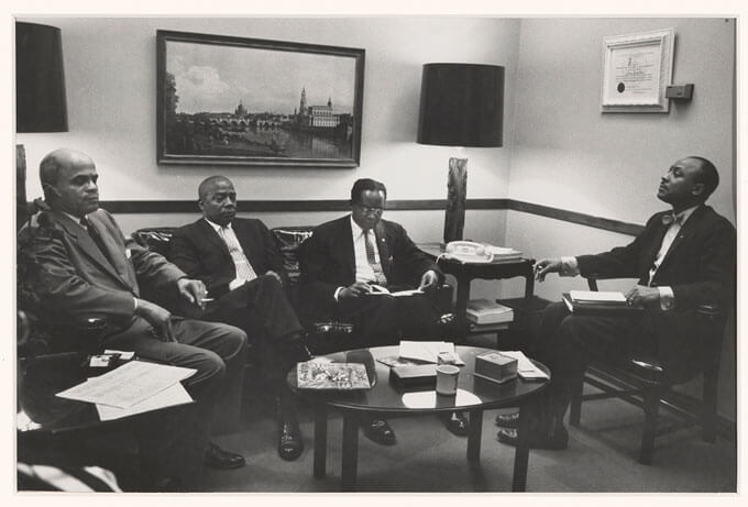 Four African American men in suits sit around a coffee table.