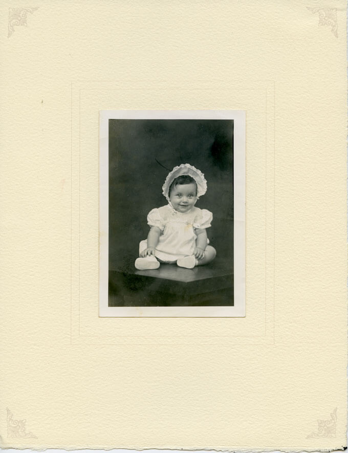 Infant girl in bonnet seated on table
