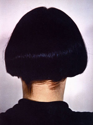 Tightly cropped portrait of a person facing away from viewer with bobbed black hair wearing a black shirt 