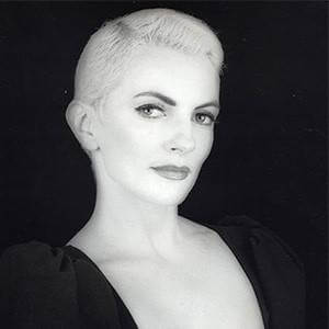 A photograph a woman with short, light hair, wearing a black blouse with a plunging neckline.