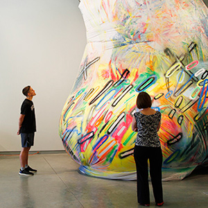 Two people view a large, colorful artpiece in the gallery.